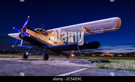 Vecchio aereo classico vintage su un piccolo campo d'aviazione di notte con cielo limpido. Biplanare abbandonato in lunga esposizione sotto le stelle Foto Stock