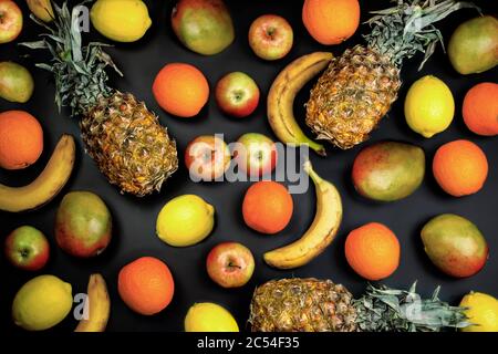 layout piatto di frutta tropicale, su sfondo nero. Frutta fresca: Mango, ananas, banana, arancia, limone. Foto Stock