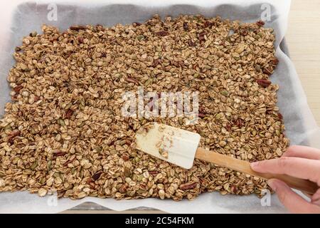 Mano femminile che stese la granola fatta in casa in Sheet Pan per cuocere Foto Stock