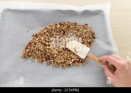 Mano femminile che stese la granola fatta in casa in Sheet Pan per cuocere Foto Stock