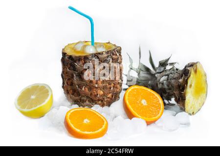 Cocktail di frutta in ananas con succo e paglia, si erge su ghiaccio, accanto ad esso si trovano un limone e un arancio Foto Stock