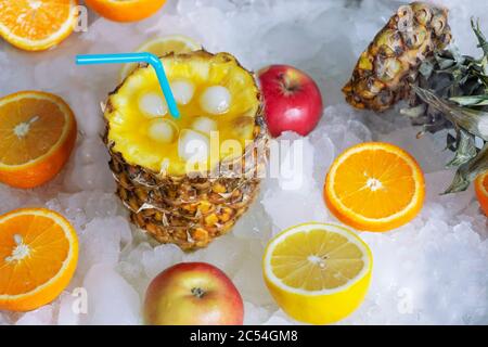 Cocktail di frutta in ananas con succo e paglia, si erge su ghiaccio, accanto ad esso si trovano un limone e un arancio Foto Stock