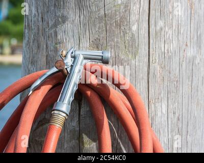 tubo rosso con ugello in metallo avvolto su un palo di legno in un molo all'aperto in una giornata di sole Foto Stock