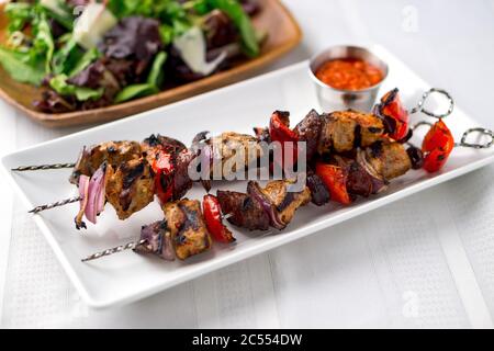 Spiedini di maiale con salsa e insalata. Questi deliziosi souvlaki di carne di maiale sono stati arrostiti sul barbecue fino a ben grigliati. Cucina cibo su spiedini ha b Foto Stock