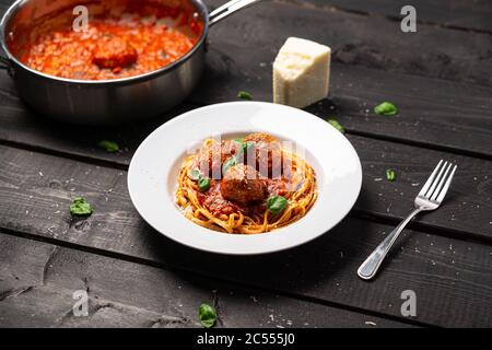 Cena con spaghetti con salsa di polpette. Piatto di pasta italiana servito in piatto bianco su fondo di legno nero. Spaghetti e polpette sono come bolognesi Foto Stock