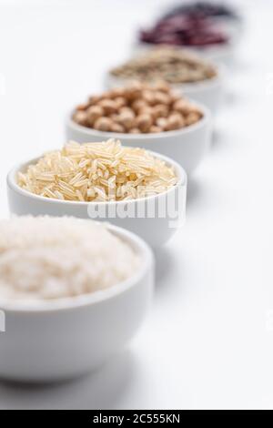 Riso Basmati chiodo di garofano lungo. Profondità di campo poco profonda sui grani di riso basmati in una ciotola bianca con altri tipi di cereali di riso e legumi di fagioli sfocati Foto Stock