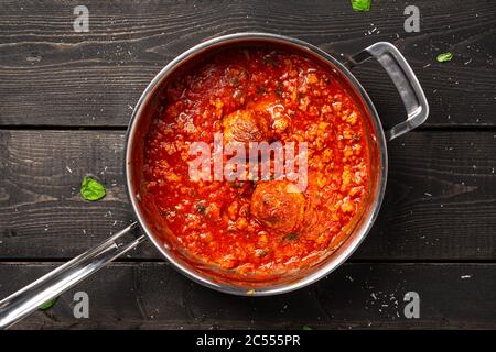 Salsa di pomodoro con polpette in padella di acciaio inossidabile. Salsa di pomodoro con polpette cotte in una pentola in acciaio inossidabile posta su uno sfondo nero scuro di legno. Questa casa Foto Stock