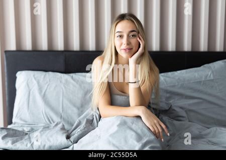 Sorridente giovane donna seduta sul letto e guarda lontano Foto Stock