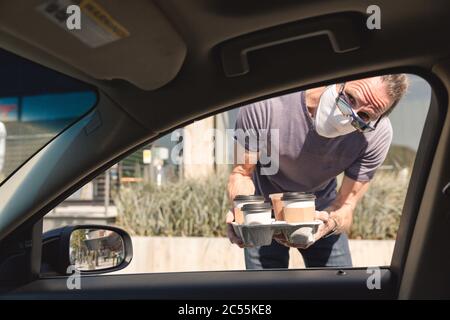 L'uomo consegna i caffè da portare fuori al finestrino di un'auto nel raccoglitore lato marciapiede Foto Stock
