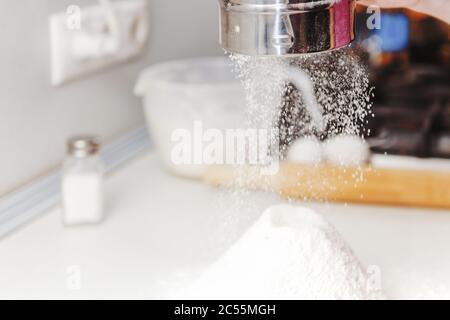 Le mani cuoce da vicino. Setacciare a mano la farina attraverso il setaccio, la farina che cade è congelata. La farina cade in movimento sul tavolo. Setacciare la farina. Baker vaglia il fl Foto Stock