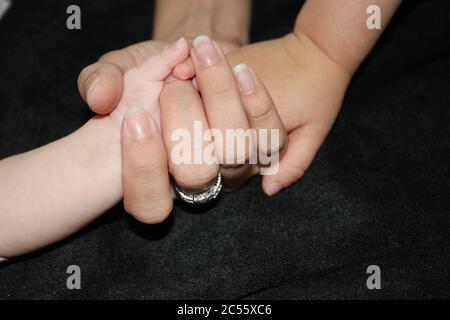 Momento tenero della mano della madre che tiene la mano del neonato su un bacground nero. Foto Stock