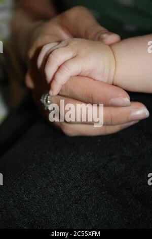 Momento tenero della mano della madre che tiene la mano del neonato su un bacground nero. Foto Stock