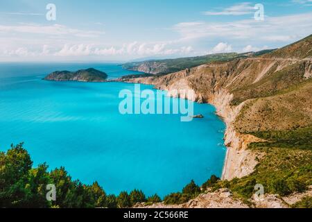 Cefalonia costa occidentale. Assos villaggio e penisola di Frourio. Bella baia blu con rocce calcaree marroni e nuvole bianche all'orizzonte. Grecia. Foto Stock