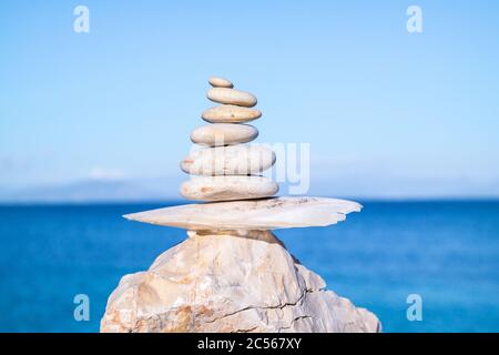 Colpo di closeup di ciottoli impilati l'uno sull'altro in un equilibrio con il mare blu sullo sfondo Foto Stock