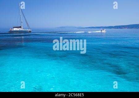 Vacanza. Laguna blu azzurro con onde calme e catamarano a vela con barca a vela con costa sullo sfondo. Foto Stock