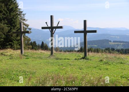 Scatto a livello di occhi di tre croci di legno su montagne verdi coperte in foreste lussureggianti Foto Stock