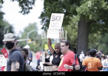 Giovane donna vista tra la folla di manifestanti che reggono il poster che dice Black Lives materia Foto Stock