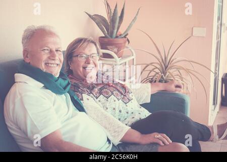 Allegro vecchio anziano giovane coppia felice sedersi sul divano a casa insieme sorridente e stare bene guardando la macchina fotografica per una famiglia ritratto - rel Foto Stock