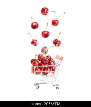 Ciliegie dolci mature che cadono in un carrello giocattolo in miniatura isolato su sfondo bianco. Concetto di shopping di frutta biologico e senza peso. Foto Stock
