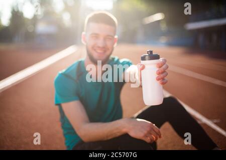 Primo piano uomo che mostra una bottiglia di sport sulla fotocamera sul circuito dello stadio Foto Stock