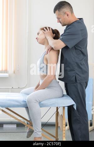 Giovane donna che ha un trattamento osteopatico - donna seduta sul divano e il maestro regola il collo. Scatto medio Foto Stock