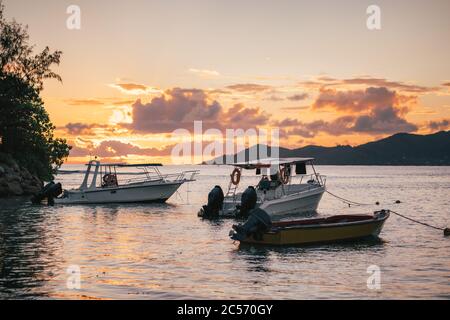 Barche da pesca riposate al tramonto luce sera vicino al porto di la Digue Island, Seychelles. Isola di Praslin all'orizzonte. Foto Stock