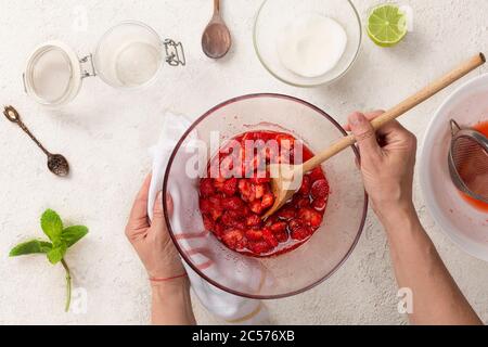 La donna sta preparando la marmellata di fragole. Mescolare le fragole con lo zucchero, vista dall'alto Foto Stock