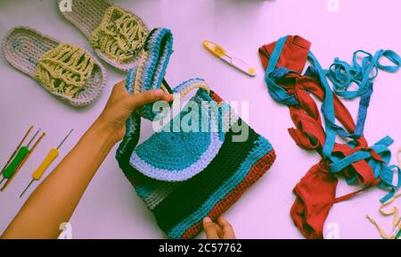 Primo piano dalla vista dall'alto donna mano tenere colorato borsa fatta a mano da riciclare vecchia t camicia su sfondo bianco, riutilizzare i vestiti da taglio in filati poi uncinetto Foto Stock