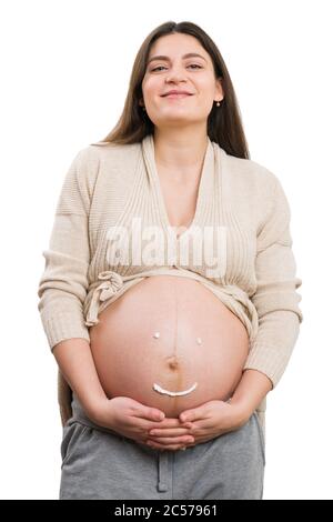 Mamma innocente futura che tiene la sua pancia con crema faccia sorridente disegnando su di esso isolato su sfondo bianco studio Foto Stock