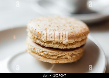 Una foto ravvicinata di un macaron con caramello salato su un piatto bianco, una tazza di caffè sullo sfondo Foto Stock