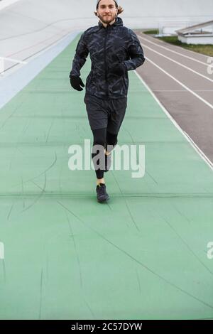 Immagine ritagliata di un giovane sportivo sicuro che corre sulla pista da corsa all'aperto Foto Stock