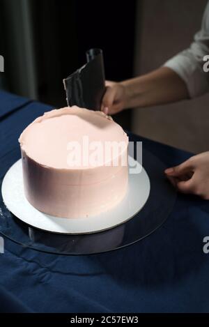 Chef Pasticceria ragazza, fa una torta di nozze con le proprie mani e spreme la crema sugli strati della torta. Foto Stock