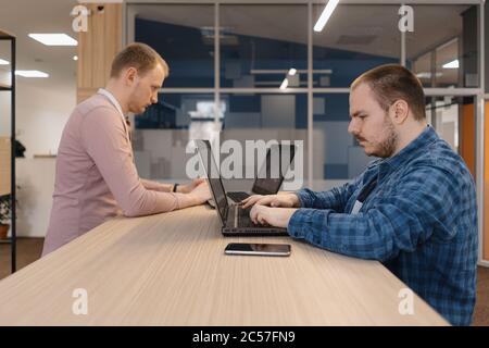 Due codificatori IT che lavorano sul notebook in piedi al tavolo in ufficio Foto Stock