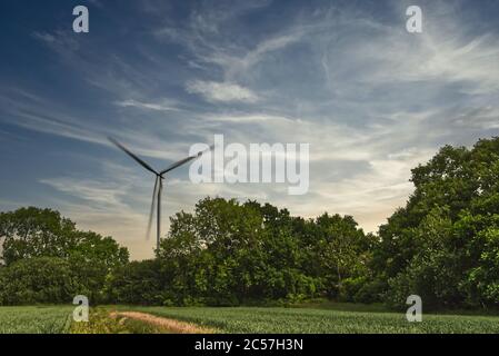 La turbina eolica rotante genera elettricità nella campagna inglese contro un cielo al tramonto Foto Stock
