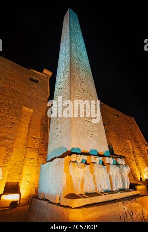 Grande obelisco con statue all'ingresso pilone all'antico tempio egiziano Luxor illuminato durante la notte Foto Stock