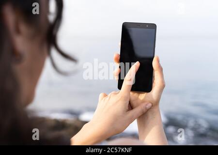 Primo piano sfocato della testa di una donna che guarda il suo telefono cellulare che tiene nella sua mano destra e tocca lo schermo con il dito della sua sinistra ha Foto Stock