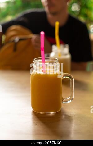 Mango fresco il succo in una tazza di plastica con il fiore di frangipani. Tropic rinfreschi. Foto Stock