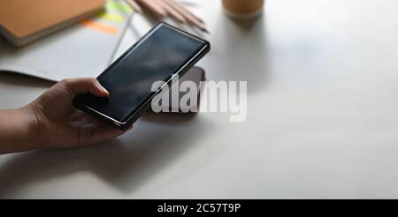 Una mano sta mettendo un telefono cellulare su un caricabatteria wireless sopra il tavolo come sfondo. Foto Stock