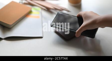 Una mano sta mettendo un telefono cellulare su un caricabatteria wireless sopra il tavolo come sfondo. Foto Stock