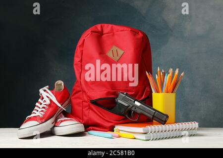 Accessori per la scuola e pistola su tavolo di legno bianco. Violenza scolastica Foto Stock