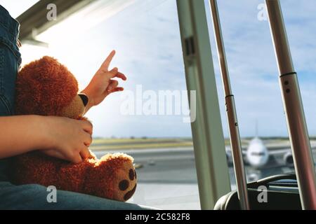 Un dito corto che punta verso il cielo e mostra l'aereo alla figlia mentre aspetta al terminal dell'aeroporto. Famiglia seduta vicino a un w Foto Stock