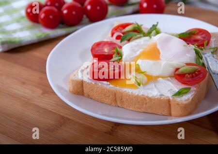 Una deliziosa colazione con uova in camicia, pane, pomodori ciliegini, formaggio ed erbe. Uova in camicia per colazione. Sandwich con formaggio, pomodori ciliegini rossi Foto Stock