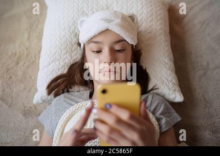 Cute teen girl si svegliò la mattina a casa e utilizzando smartphone Foto Stock