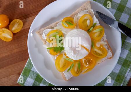 Una deliziosa colazione con uova in camicia, pane, pomodori ciliegini gialli, formaggio ed erbe. Uova in camicia per colazione. Sandwich con formaggio, ciliegia gialla Foto Stock
