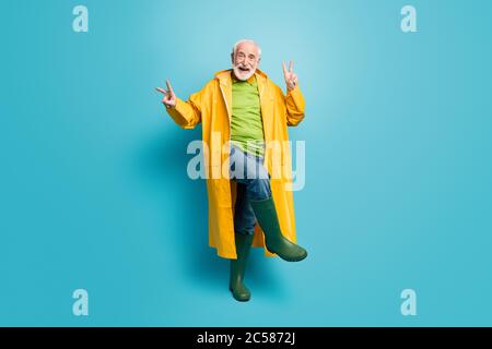 Vista a lunghezza intera del corpo del suo bel ragazzo allegro e allegro uomo con capelli grigi che indossa cappotto danzante mostrando doppio segno V buon umore isolato su luminoso Foto Stock