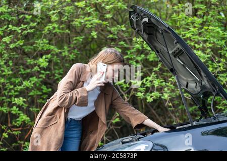 Una donna impotente che ha chiesto aiuto/assistenza per cercare un'auto rotta, si è fermata sul lato della strada. Non capisce cosa è successo. Foto Stock