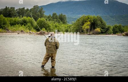 Un pescatore che lotta un salmone mentre guai sul fiume Kitimat nella Columbia Britannica, Canada, con il verga piegato e la foresta e le montagne nel backgro Foto Stock