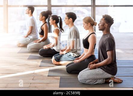 Concetto di benessere. Giovani sportivi in classe yoga facendo insieme esercizi di meditazione Foto Stock