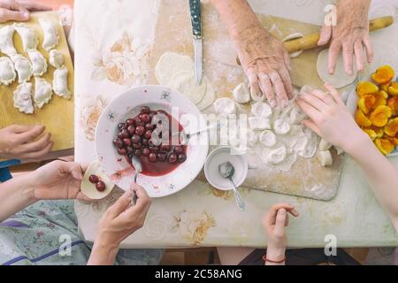 Vista dall'alto del tavolo da cucina con le mani di una famiglia irriconoscibile che prepara gnocchi fatti in casa, stile di vita reale, vista dall'alto. Cucina tradizionale nazionale Foto Stock
