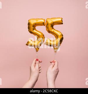 Mano femminile che tiene un numero 55 compleanno anniversario celebrazione palloncino oro Foto Stock